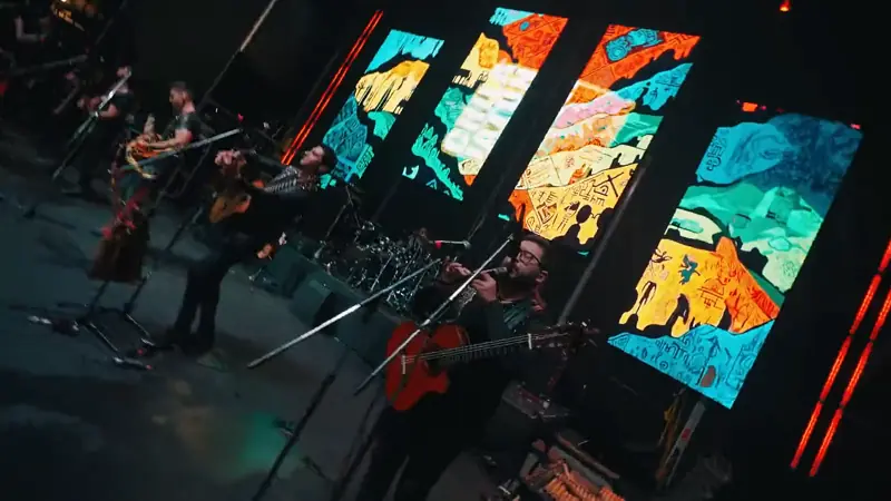 Banda tocando frente a pantallas con arte andino